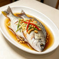 Steamed whole yellowfin sea bream plated in sauce with chilli and spring onion