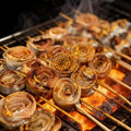 Hairtail rolls grilling on a charcoal skewer rack with a savoury glaze